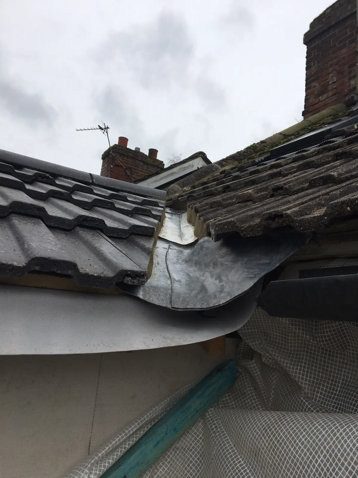 New lead flashing dressed over a tile course where a roof meets a higher wall, chimney behind