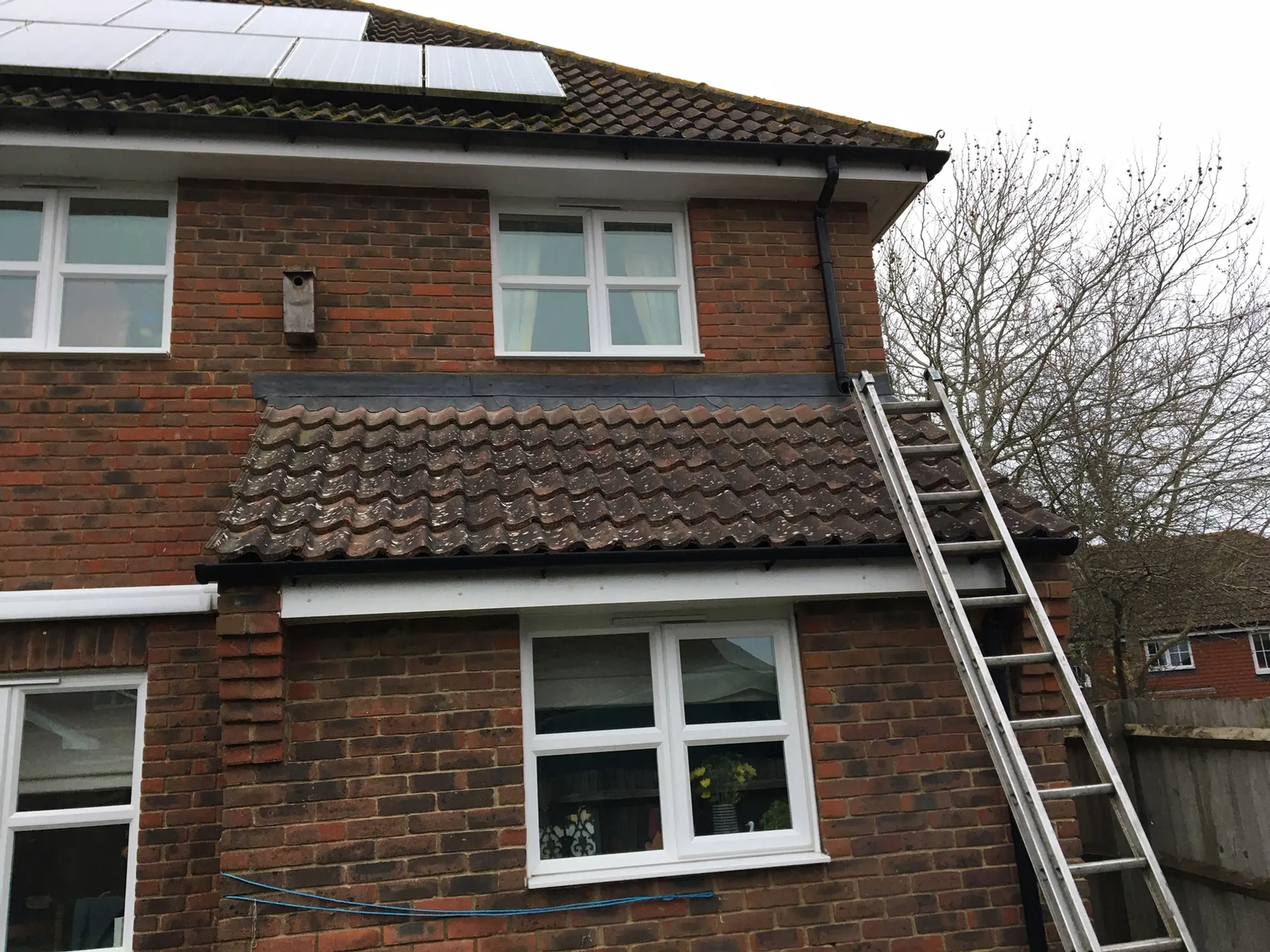 A red brick house with a tiled roof, a ladder up the side and a solar panel