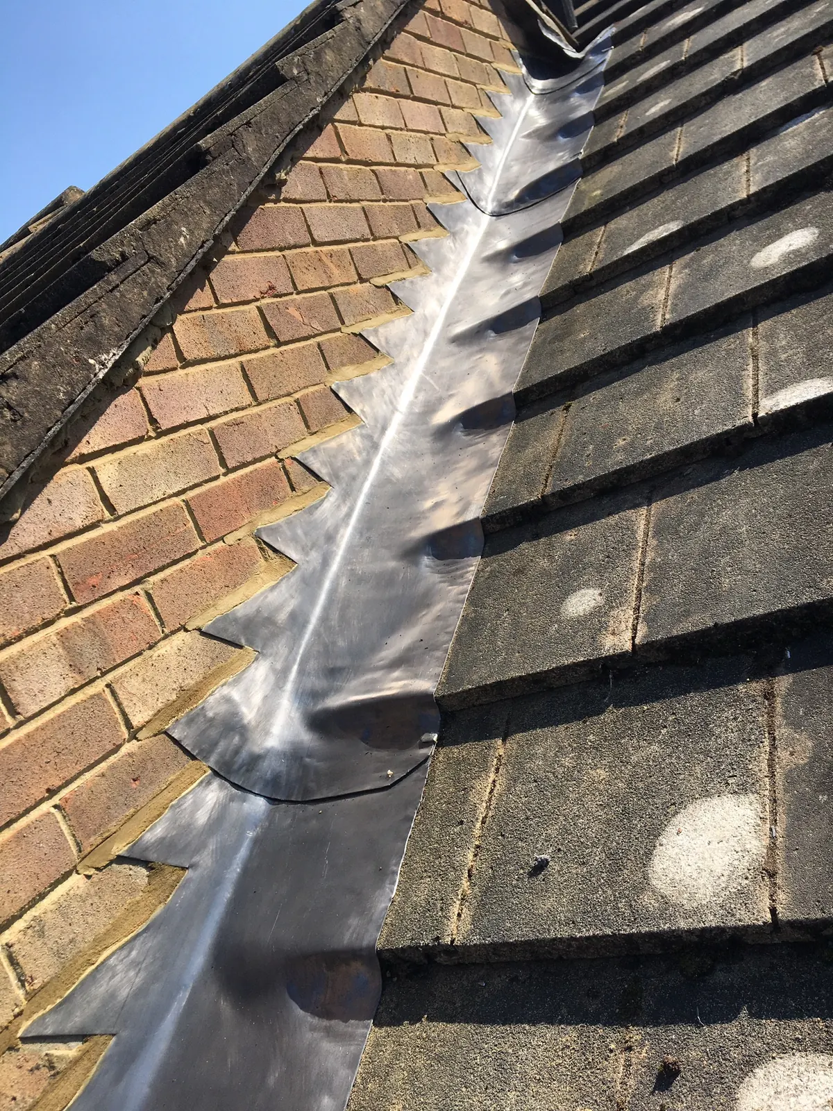 A lead valley gutter running between a brick wall and a tiled roof in full sun