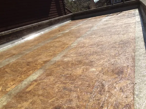 The weathered surface of an old fibreglass flat roof, trim visible along the edge