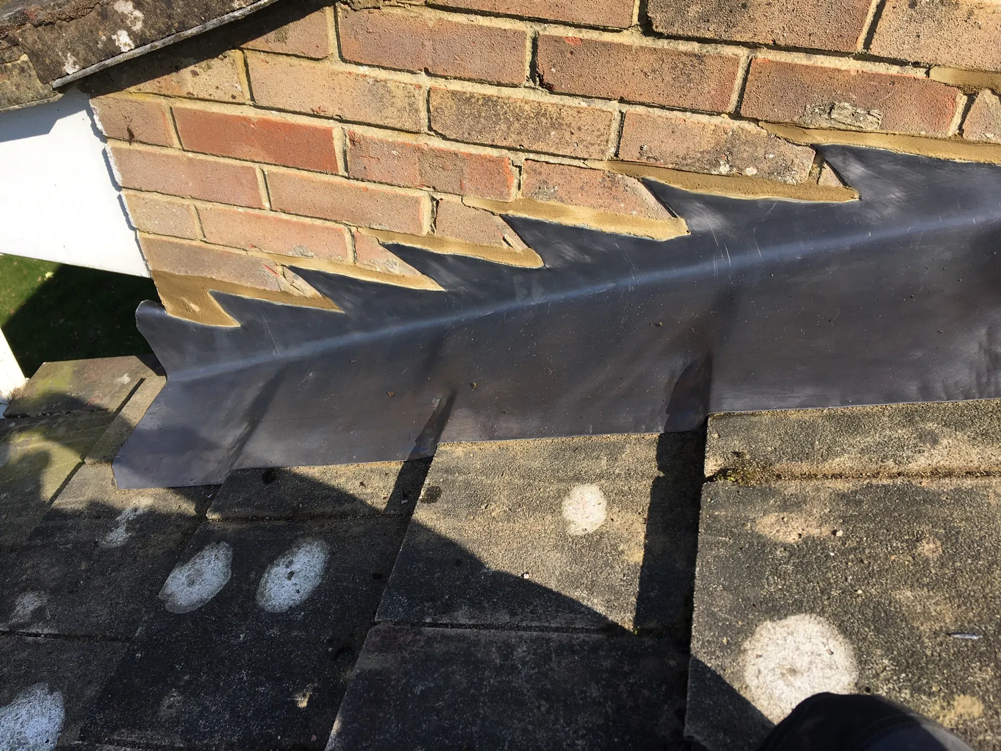 Stepped lead flashing let into brickwork where a tiled roof runs into a gable wall