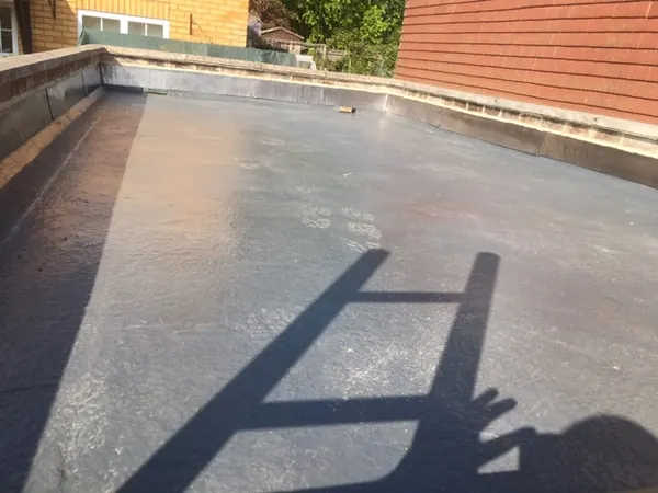 A flat roof with the roofer's own shadow and the shadow of his ladder falling across it