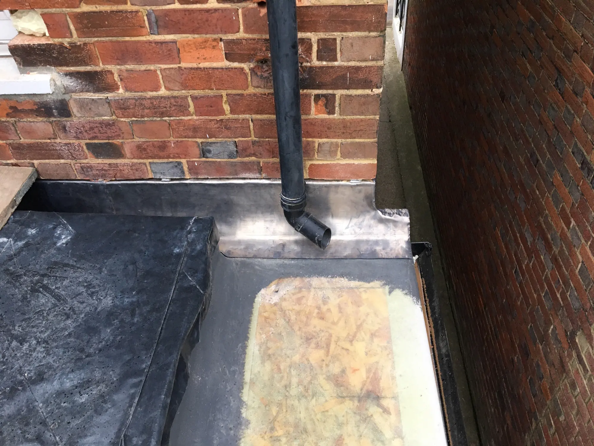 A lead-lined gutter between two brick walls with a black downpipe discharging onto it