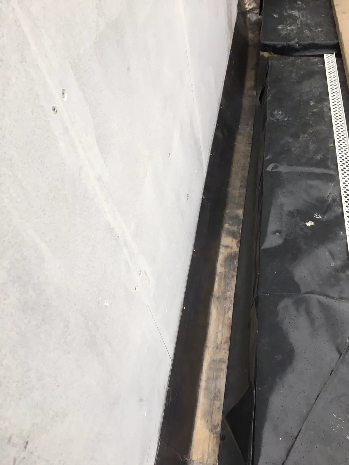 A lead-lined box gutter behind a rendered wall with a mesh leaf guard along it