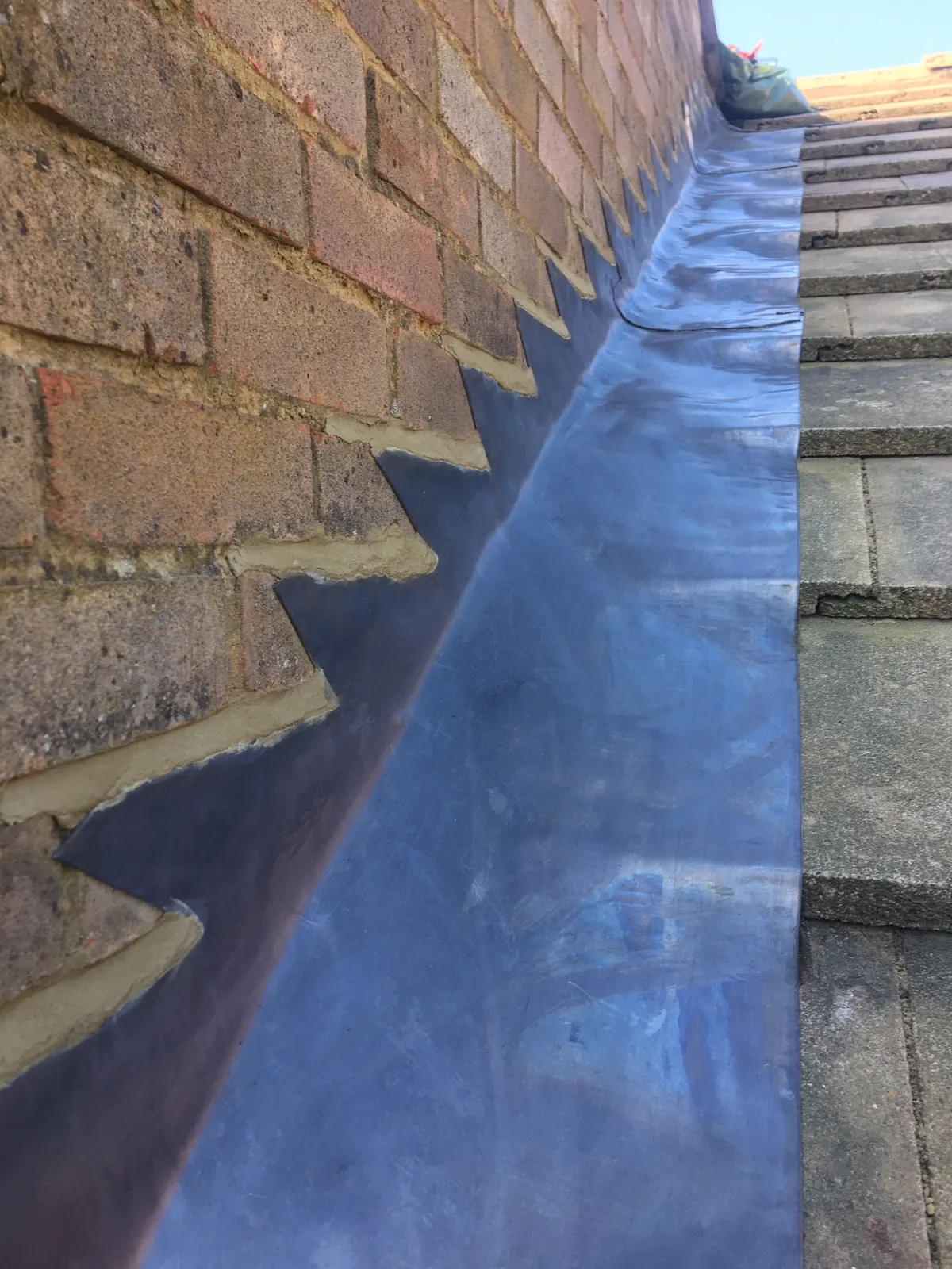 Stepped lead flashing climbing a brick wall beside newly dressed lead and a tiled roof