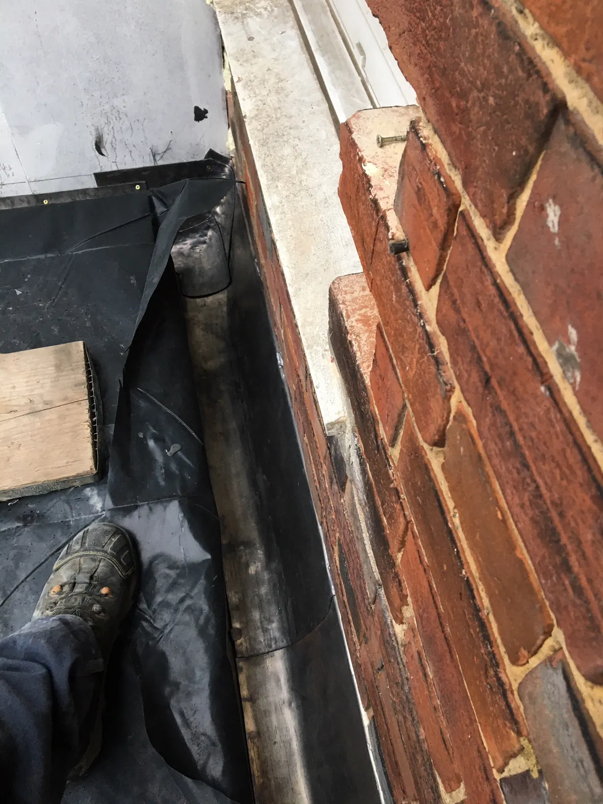 The roofer's boot planted in a lead-lined gutter beside brickwork and a downpipe